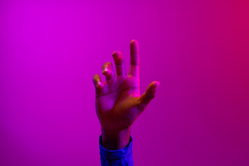 Hand of caucasian businessman pointing with copy space on neon pink to purple background