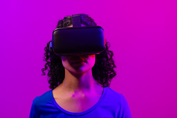 Biracial woman using vr headset on neon pink to purple background