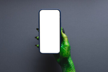 Green monster hand holding smartphone with copy space on grey background