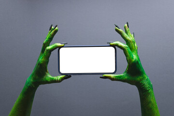 Green monster hands holding smartphonewith copy space on grey background