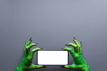 Green monster hands holding smartphone with copy space on grey background