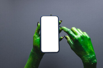 Green monster hand holding smartphone with copy space on grey background