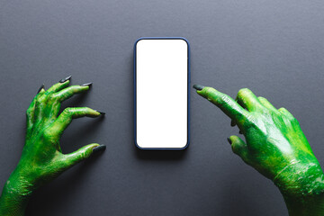 Green monster hands pointing on smartphone with copy space on grey background