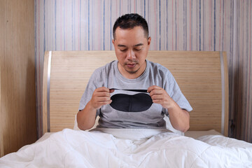 Asian man get ready to sleep wearing eye mask in bed at home