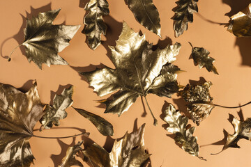 Metallic gold autumn leaves lying on orange background