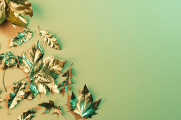Fototapeta premium Metallic gold autumn leaves with copy space on green background