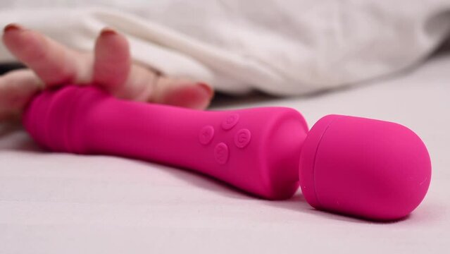 Woman taking pink vibrator lying under white blanket. 