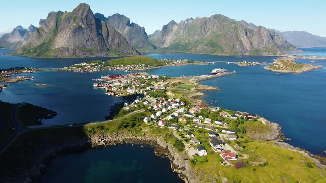 A traditional fishing village in northern Norway on a sunny summer day, blue lagoon and high mountain peak - Aerial Shot.