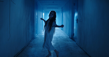Little girl in white dress looking like a ghost carelessly dancing in the hallway of a haunted...