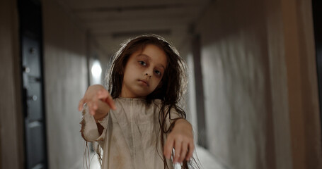 Little caucasian girl in ghost white sundress costume for halloween stretching her arms into...