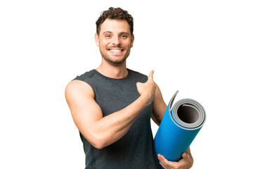 Young sport man going to yoga classes while holding a mat over isolated chroma key background pointing back - obrazy, fototapety, plakaty