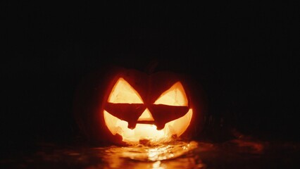 A pumpkin for Halloween on the beach by the sea, candles are burning inside, it is washed away by a wave. Close-up.