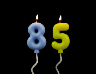 Air balloon shaped burning birthday candles isolated on black background, number 85.