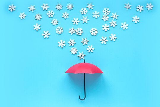 Various wooden snowflakes shape fall onto a red umbrella on blue background.