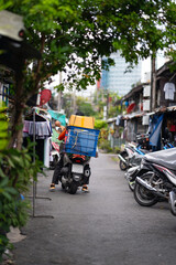 A scooter driver loaded with boxes drives away a narrow street.