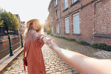 follow me concept - happy smiling woman holding hand of girlfriend in old downtown street
