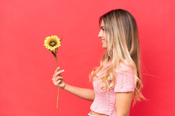 Obraz na płótnie Canvas Young pretty Uruguayan woman holding sunflower isolated on background with happy expression