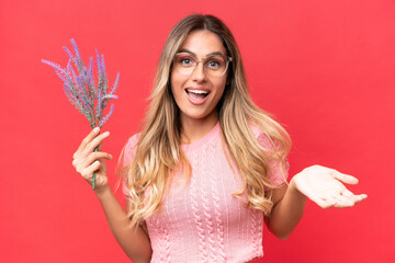 Young pretty Uruguayan woman holding lavender isolated on red background with shocked facial...