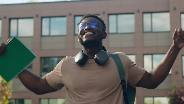Happy winner successful African American university college academy student guy man male walking outdoors in city education success learning good results win achieve test exam studying achievement