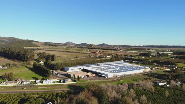 Drone footage captures a factory from an aerial side view, showcasing the harmonious blend of industrial infrastructure with the natural beauty of rolling hills and lush greenery