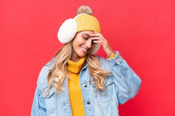 Young pretty Uruguayan woman wearing winter muffs isolated on red background background laughing