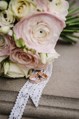 Wedding rings bride and groom with bridal bouquet white and pink flowers roses. Two beautiful golden wedding rings. Mens, womens ring with ornament. Close Up. Engagement.