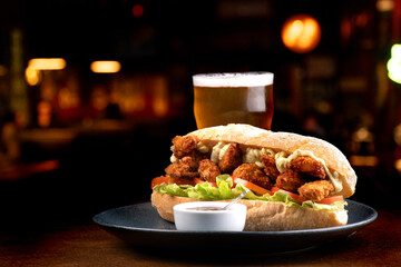large sub sandwich of fried chicken breaded with lettuce tomato and mayonnaise with a pint of beer...