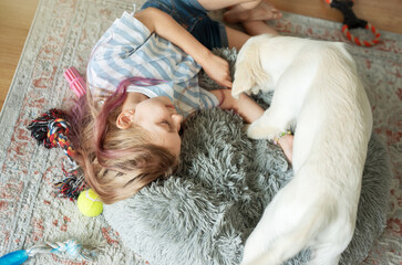 Little girl playing with a golden retriever puppy at home.