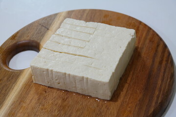 A block of tofu on a round wooden cutting board