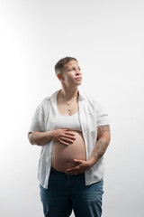 A pregnant woman shows off her big baby bump, protectively holding her pregnancy belly with both hands. Adding narrative, she is lesbian, married, and has a fresh, stylish butch aesthetic.
