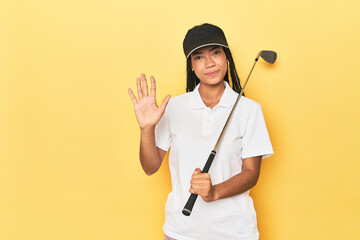 Indonesian female golfer on yellow backdrop smiling cheerful showing number five with fingers.