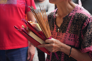 As chanting and gongs resonate, a devotee holds joss sticks and spirit money in prayer. Chinese Folk Rituals for Traditional Festivals.