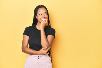 Young Indonesian woman on yellow studio backdrop relaxed thinking about something looking at a copy space.