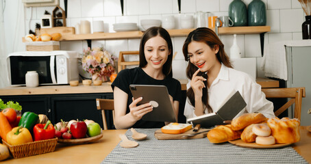 Two beautiful woman in the kitchen in an apron, fresh vegetables on the desk, writes down her favorite recipes, comes up with ideas for dishes