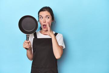 Woman with apron and pan on blue background is saying a secret hot braking news and looking aside