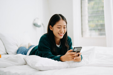 Beautiful young asian woman on a white bed with coffee cub and using smart phone at home. lifestyle concept