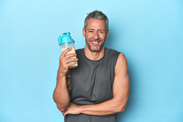 Athlete holding protein shake on blue backdrop laughing and having fun.