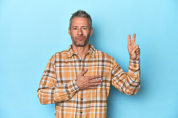 Middle-aged caucasian man on blue backdrop taking an oath, putting hand on chest.