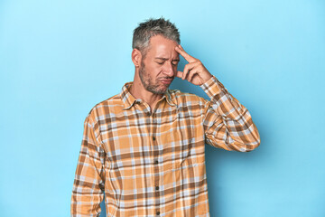 Fototapeta premium Middle-aged caucasian man on blue backdrop having a head ache, touching front of the face.