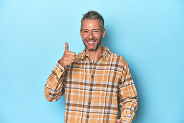 Fototapeta premium Middle-aged caucasian man on blue backdrop raising both thumbs up, smiling and confident.