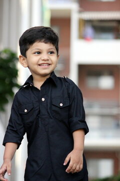 Cute little toddler boy in Black Pathani outfit. Adorable boy is standing and smiling. Looking at someone and expressing his joy. Feastival, bollywood look of a smart boy in a day light. 
