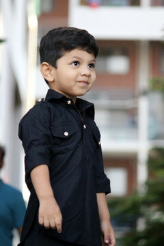 Cute and curious boy standing and looking at someone, He is wearing black pathani kurta and in a festive mood. adorable child with naughty expression standing outdoor. handsome black pathani outfit.