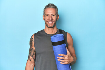 Athlete holding a fitness mat on blue studio background © Asier