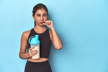 Young athlete with protein shake, ready for gym with fingers on lips keeping a secret.