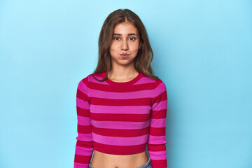 Teen girl in striped pink and red tee on blue blows cheeks, has tired expression. Facial expression...