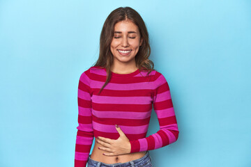 Obraz premium Teen girl in striped pink and red tee on blue touches tummy, smiles gently, eating and satisfaction concept.