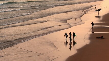 Fototapeta na wymiar Surfers Walking with Boards on Atlantic Ocean Coast at Sunset in Morocco