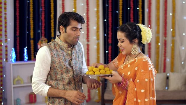 Happy Indian nuclear family celebrating the festival together - Young husband and wife feeding laddoo to each other . Indian stock footage of Diwali celebration by a young married couple at home. I...