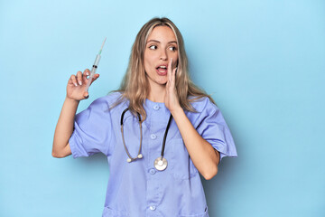 Young caucasian nurse in blue studio is saying a secret hot braking news and looking aside