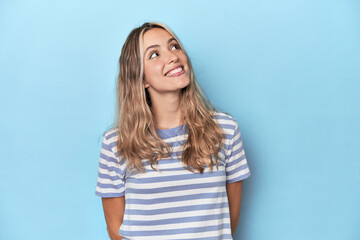 Blonde young caucasian woman in blue studio relaxed and happy laughing, neck stretched showing teeth.